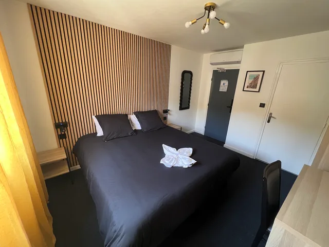 Chambre Standard avec lit Queen, têtes en bois cannelé clair, suspension dorée et porte donnant sur le couloir